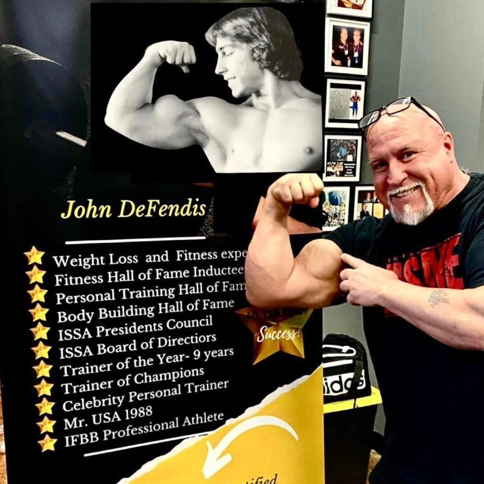 Bald man flexing bicep and smiling next to a fitness achievements display featuring John DeFendis.