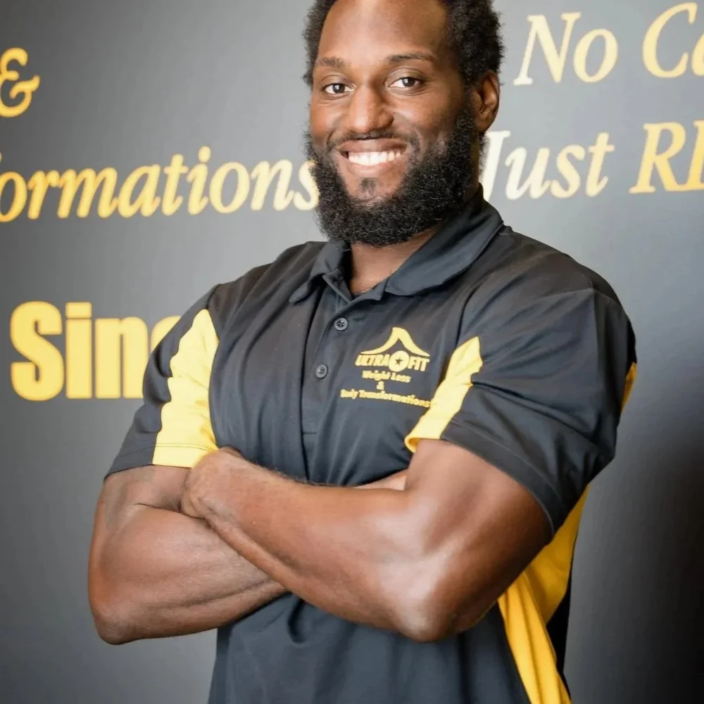 Smiling man with folded arms in a black and yellow polo shirt stands in front of a motivational wall.